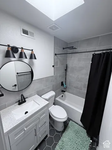 Skylight with integrated exhaust fan, modern vanity with stone countertop, hexagon tile flooring, and subway tile shower surround