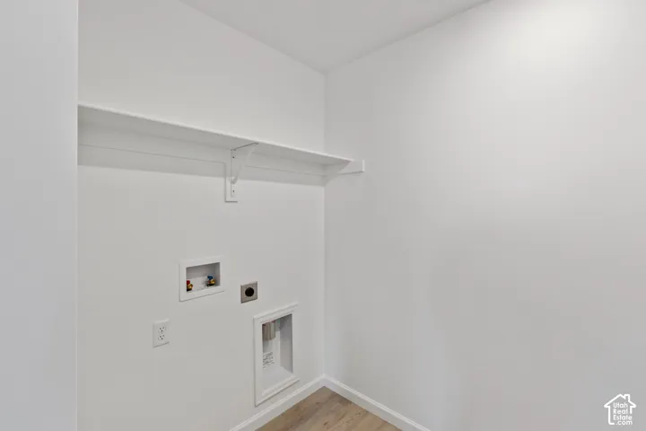 Laundry area with an overhead shelf, utility connections, and wood-finish flooring. HOME TO BE BUILT! Pictures are of another similar Spec and not of this exact home. Colors and other options may vary from those seen here. Please see Sales consultant for