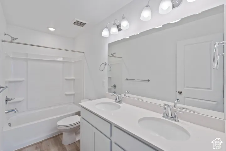 Dual sink vanity with white countertop, chrome fixtures, built-in mirror, and wood-finish flooring. HOME TO BE BUILT! Pictures are of another similar Spec and not of this exact home. Colors and other options may vary from those seen here. Please see Sales