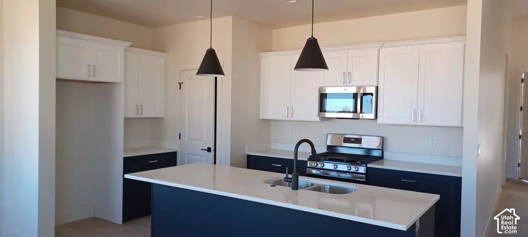 Modern kitchen featuring two-tone cabinetry, stainless steel appliances, a center island with an undermount double basin sink, and pendant lighting