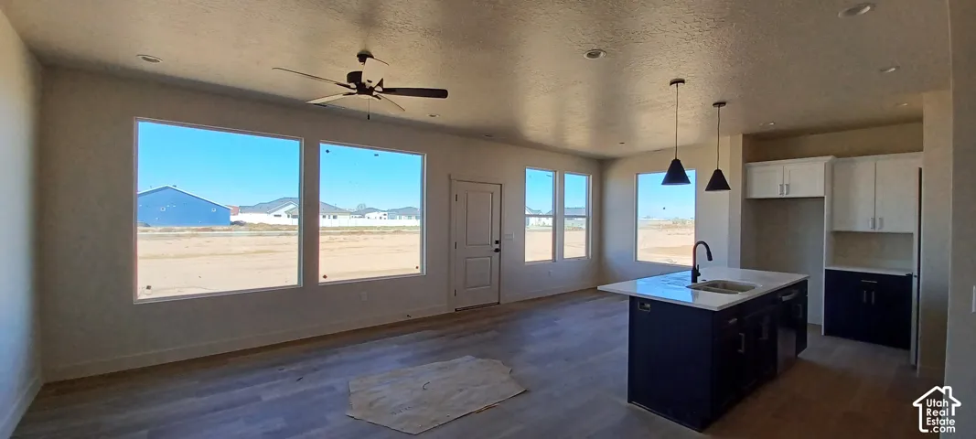 Spacious open-concept living area featuring wood-finish flooring, abundant natural light from multiple windows, a ceiling fan, and recessed lighting