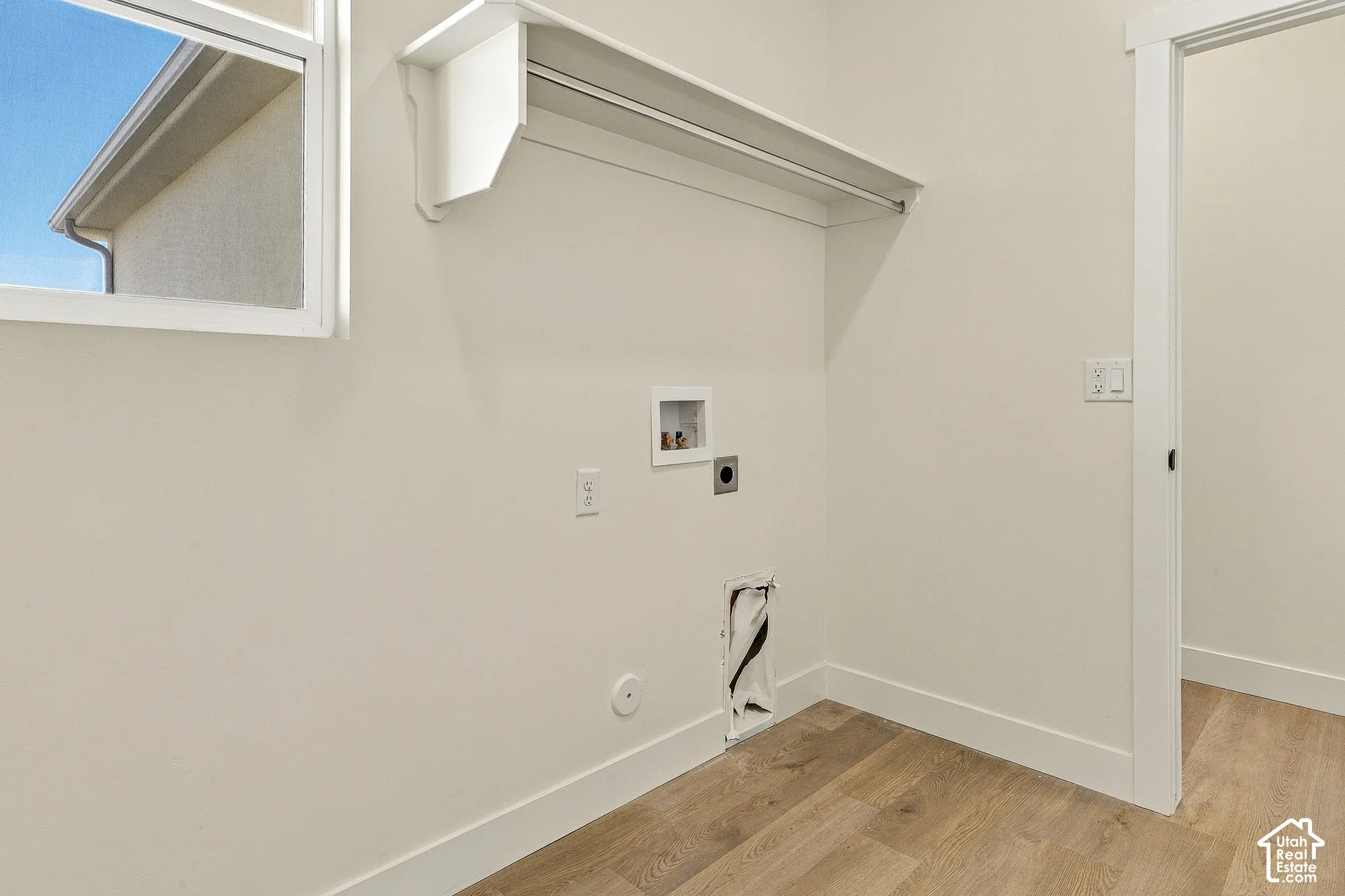 Neutral-toned utility room featuring wood-finish flooring, a single-hung window, and a built-in wall-mounted shelf with integrated clothing rod