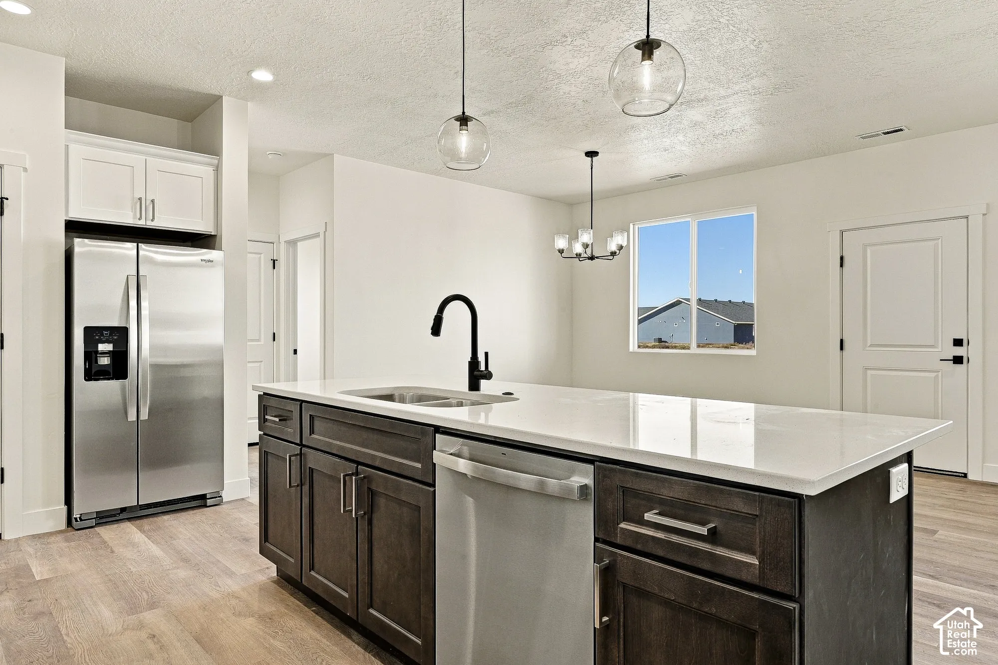 Kitchen featuring a central island with a solid-surface countertop, dark-finish cabinetry, a matte black faucet, pendant lighting, and stainless steel appliances