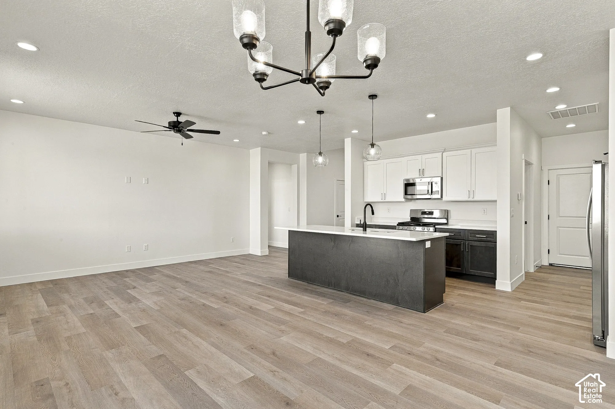 Kitchen featuring a two-tone island, light-toned wood-finish flooring, white upper cabinetry, recessed lighting, and a multi-arm chandelier