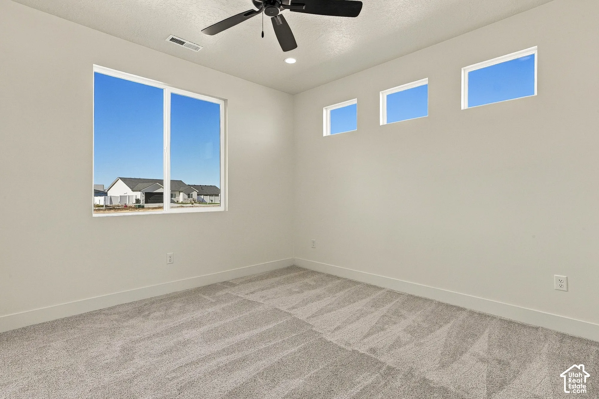 Neutral-toned carpeted flooring, vaulted ceiling, black ceiling fan, large picture window, and three elevated transom windows