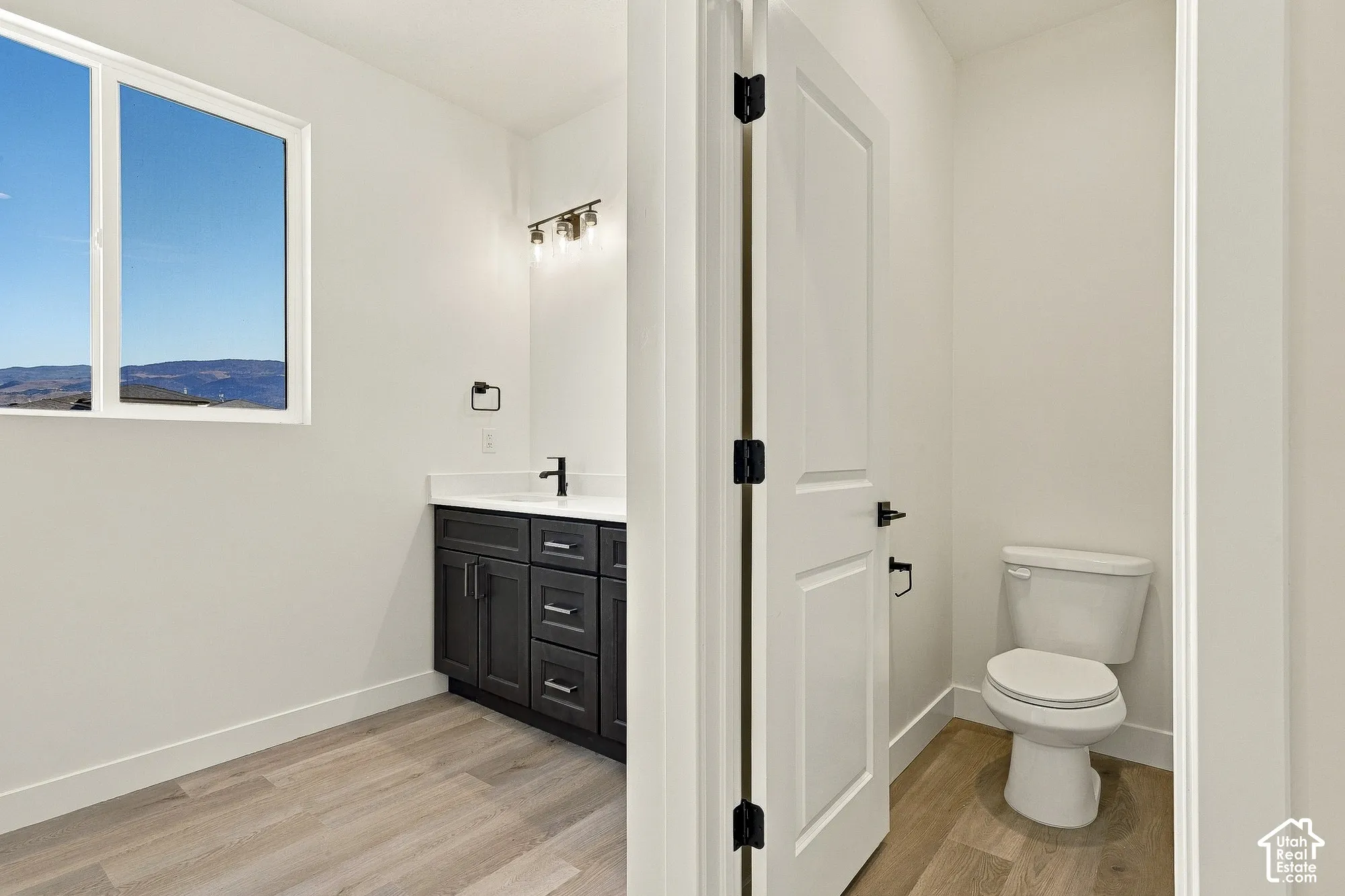 Bathroom featuring a dark wood-finish vanity, white countertop with an integrated sink, matte black hardware, and wood-finish flooring