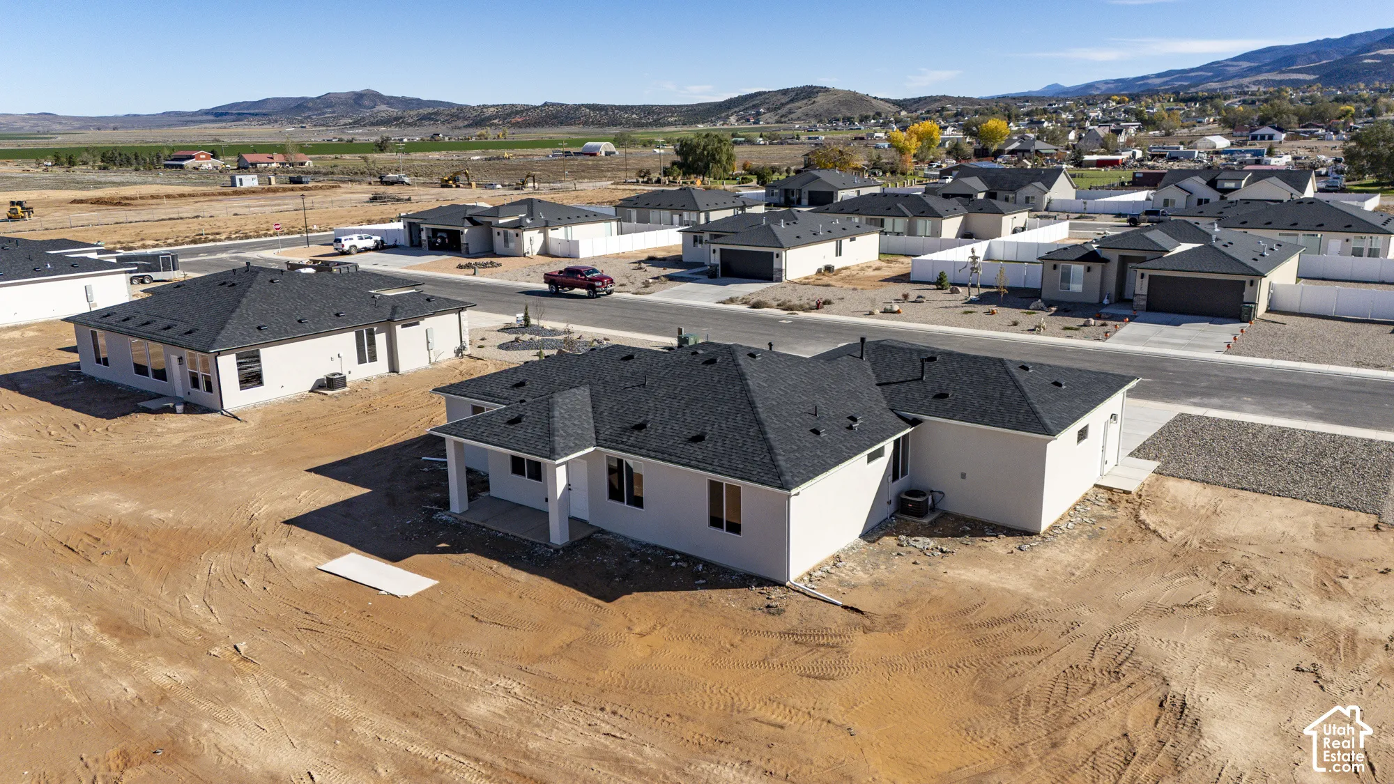 Aerial perspective of a single-story residence featuring a light-toned stucco exterior, dark asphalt shingle roof, covered rear patio, and mountain scenery