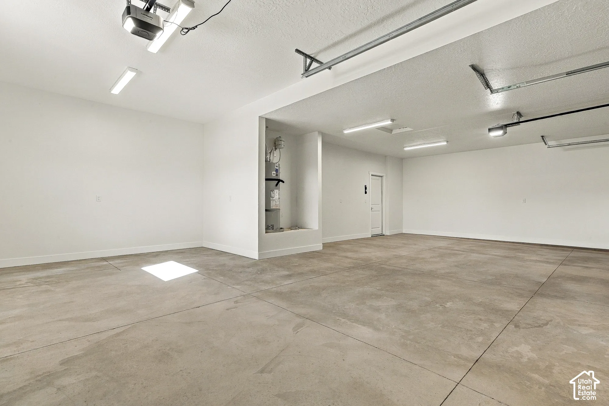 Multi-car garage featuring expansive concrete flooring, bright overhead fluorescent lighting, and a recessed water heater alcove