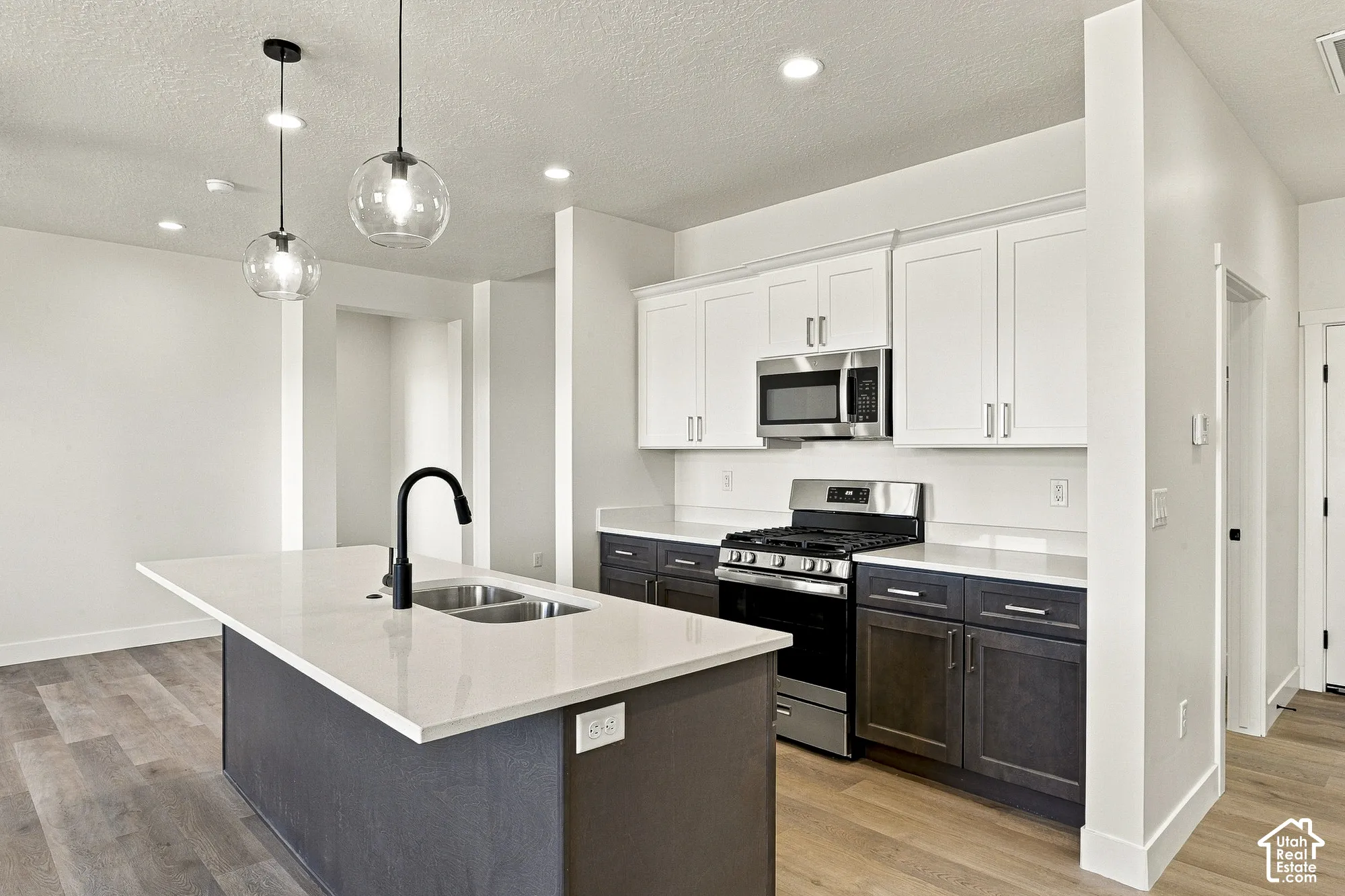 Kitchen featuring two-tone cabinetry, quartz countertops, a central island with a matte black high-arc faucet, stainless steel appliances, and wood-finish flooring