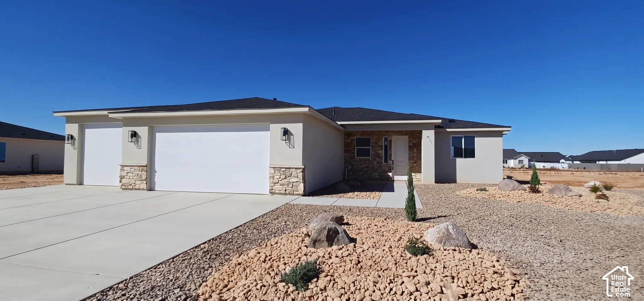 Stucco exterior with stone accents, two-car garage, concrete driveway, and a Xeriscaped front yard