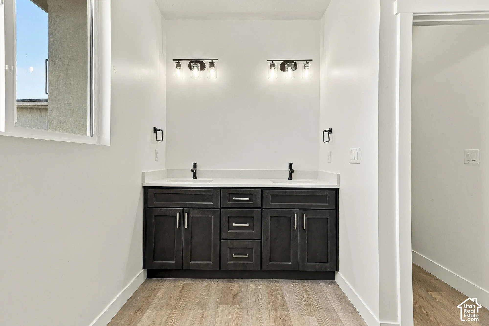 Double vanity with dark cabinetry, stone-surface countertop, rectangular undermount sinks, matte black hardware, and dual multi-light wall fixtures
