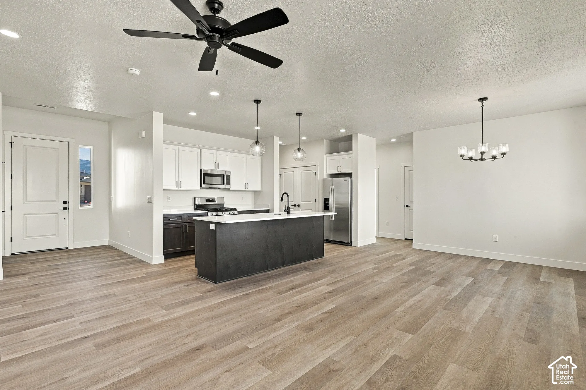 Kitchen featuring white upper cabinetry, dark lower cabinetry, quartz countertops, a central island with a matte black faucet, and wood-finish flooring