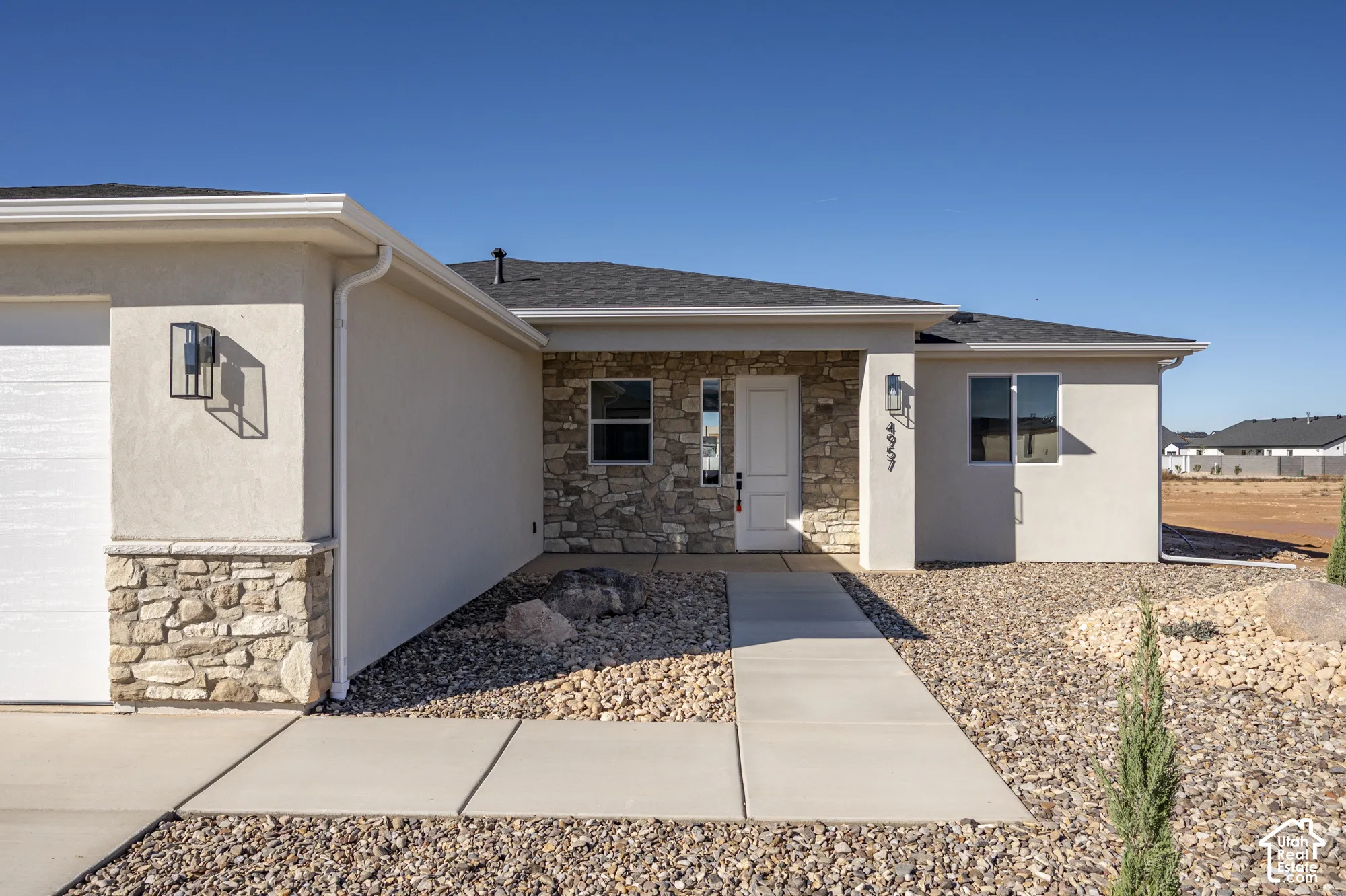 Stucco exterior featuring stacked-stone accents, covered entryway, concrete walkway, and wall-mounted exterior lighting