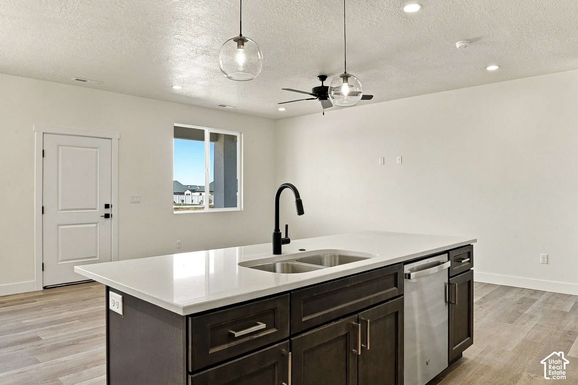 Kitchen island featuring dark cabinetry, a white countertop, a dual-basin stainless steel sink, and a matte black gooseneck faucet