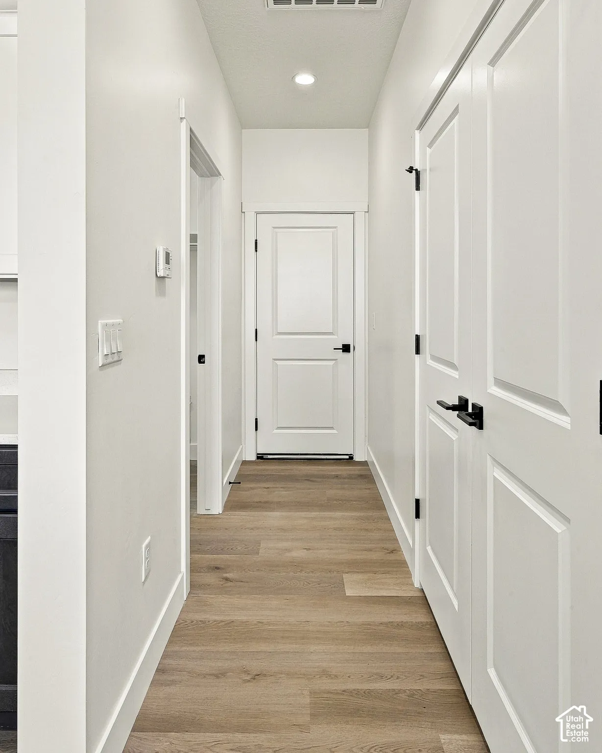 Hallway featuring wood-finish flooring, white two-panel interior doors, and matte black hardware