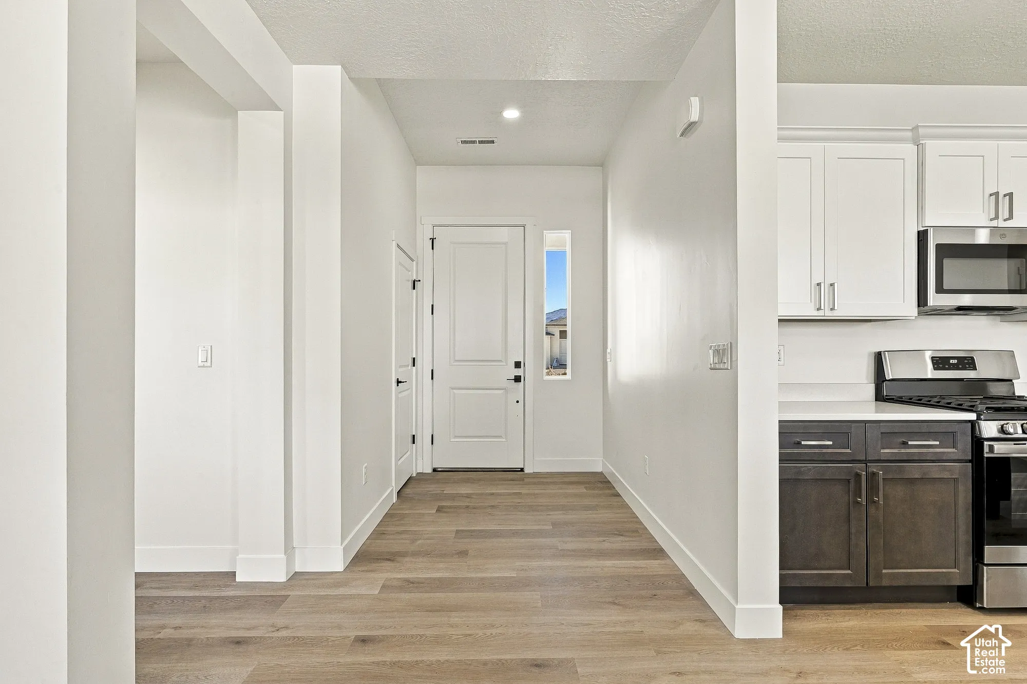 Entryway featuring a high-contrast kitchen with white upper cabinetry and dark lower cabinetry, wood-finish flooring, and a single-panel door with a vertical sidelight window