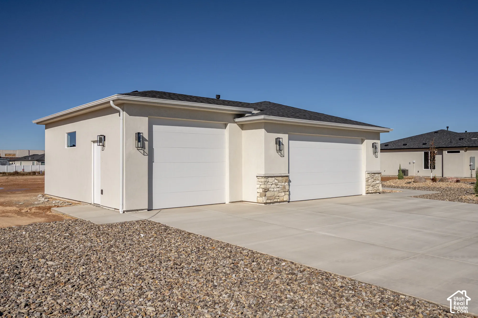 Stucco exterior featuring a three-car garage, stone masonry accents, a concrete driveway, and wall-mounted exterior light fixtures