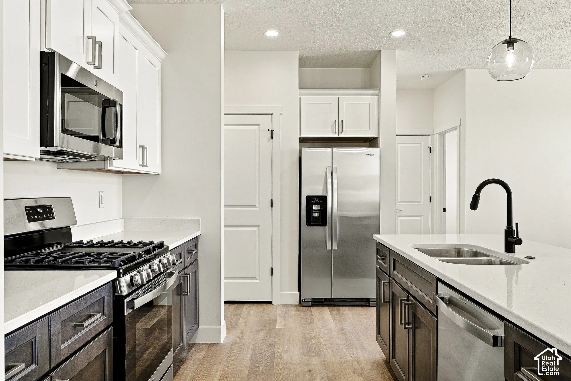 Kitchen featuring white upper cabinetry, dark wood-finish lower cabinetry, solid-surface countertops, stainless steel appliances, and a matte black gooseneck faucet