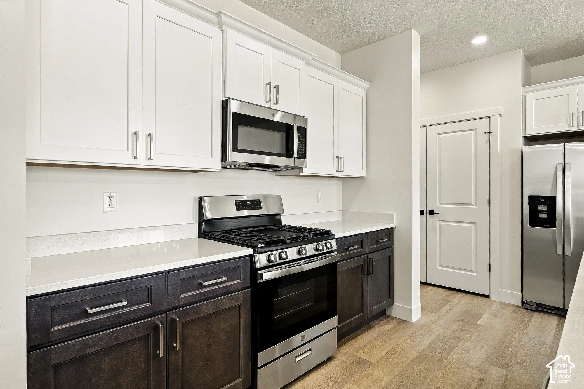 Kitchen featuring two-tone cabinetry, stone-surface countertops, stainless steel gas range with built-in microwave, and wood-finish flooring