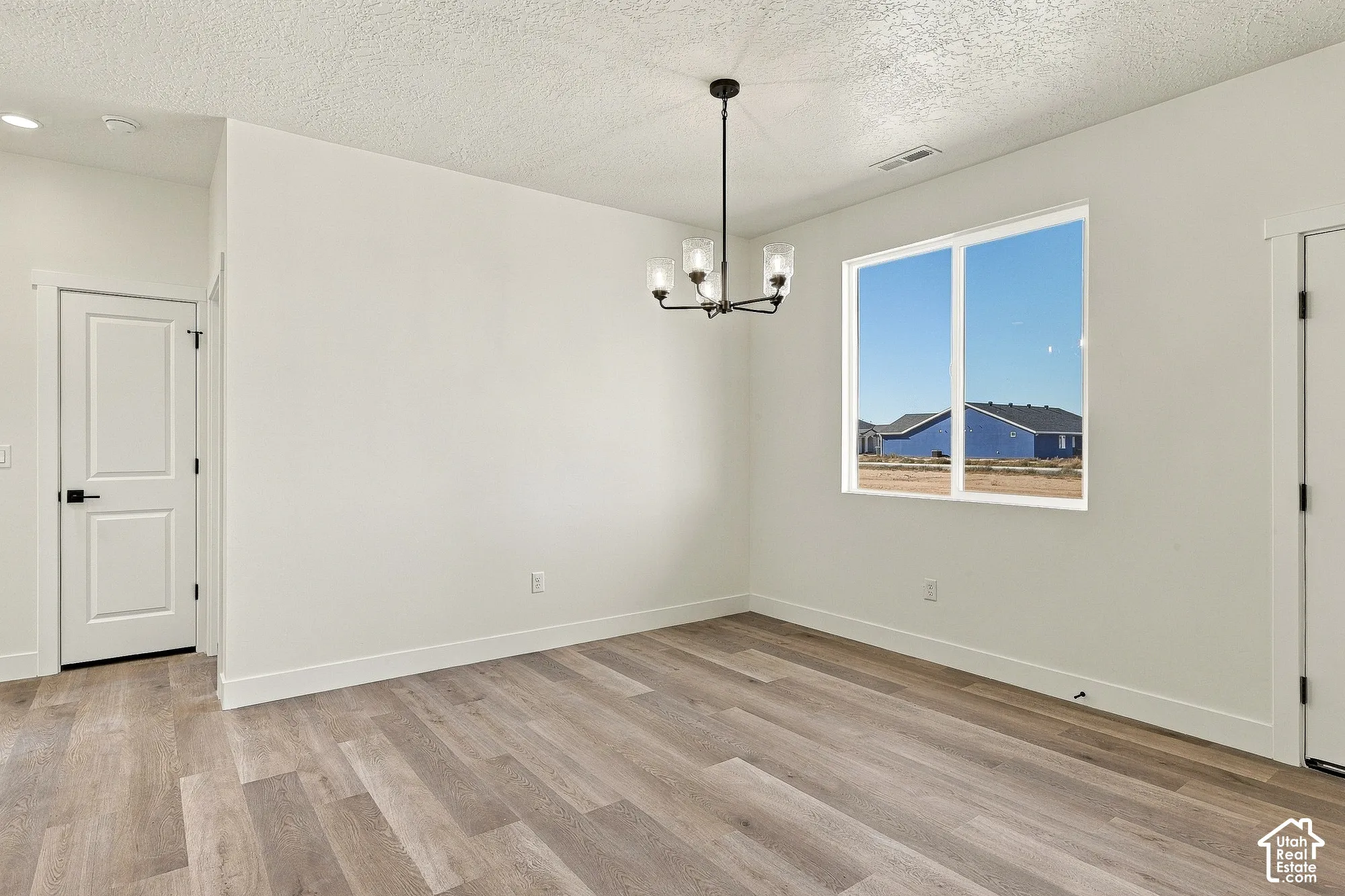Neutral interior space featuring wood-finish flooring, a multi-light metal chandelier, a large rectangular window, and paneled doors with matte black hardware