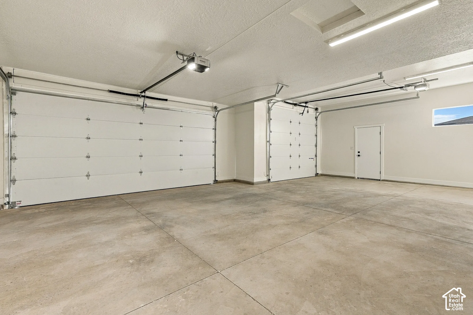 Three-car garage featuring a concrete floor, two automated garage door openers, LED strip lighting, and a separate side entry door