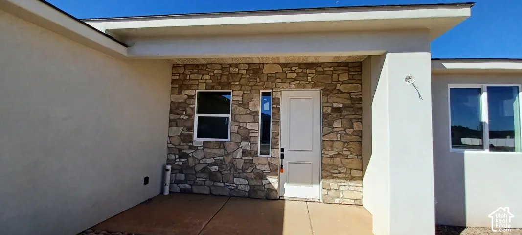 Stucco exterior with stone veneer accents, covered entry, white paneled door, and multiple windows