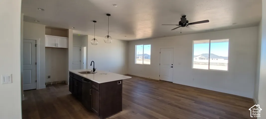 Open concept living area featuring wood-finish flooring, a kitchen island with pendant lighting, a ceiling fan, and large windows