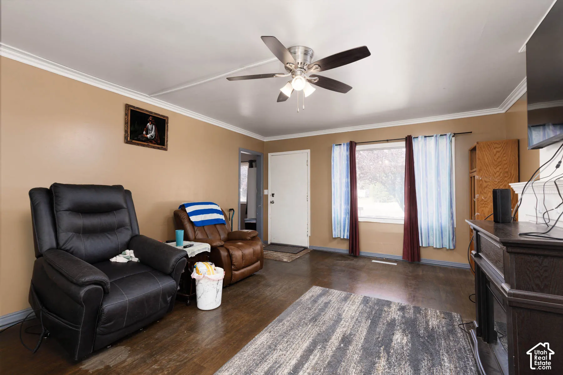Wood-finish flooring, ceiling fan with integrated lighting, crown molding, and a window with curtain rods
