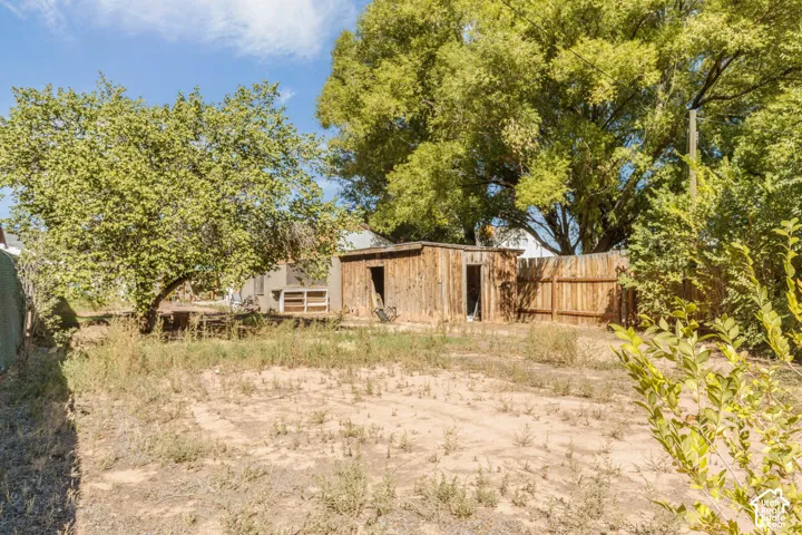 Expansive outdoor area featuring mature trees, a wood privacy fence, and a rustic wood outbuilding