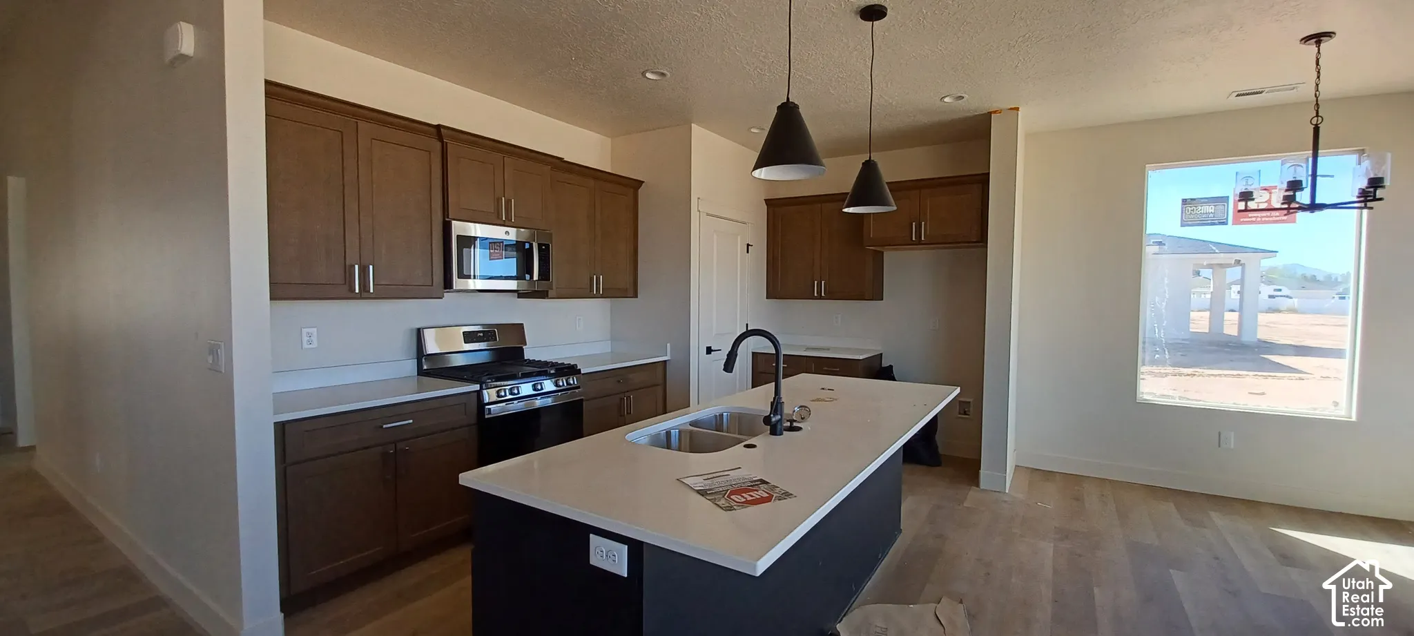 Kitchen featuring wood-finish cabinetry, stainless steel appliances, a center island with sink, and pendant lighting