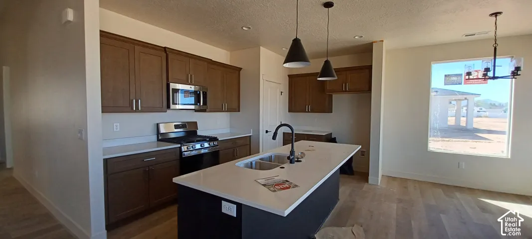 Kitchen featuring wood-finish cabinetry, stainless steel appliances, a center island with sink, and pendant lighting