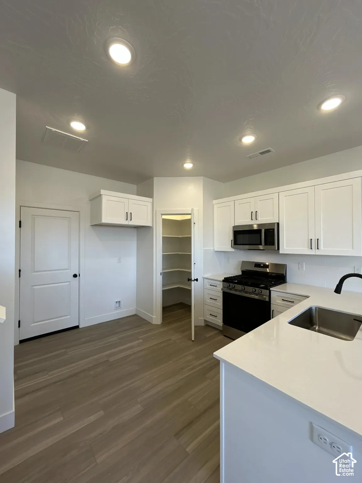 White shaker cabinetry, wood-finish flooring, stainless steel appliances, white countertops, and a walk-in pantry