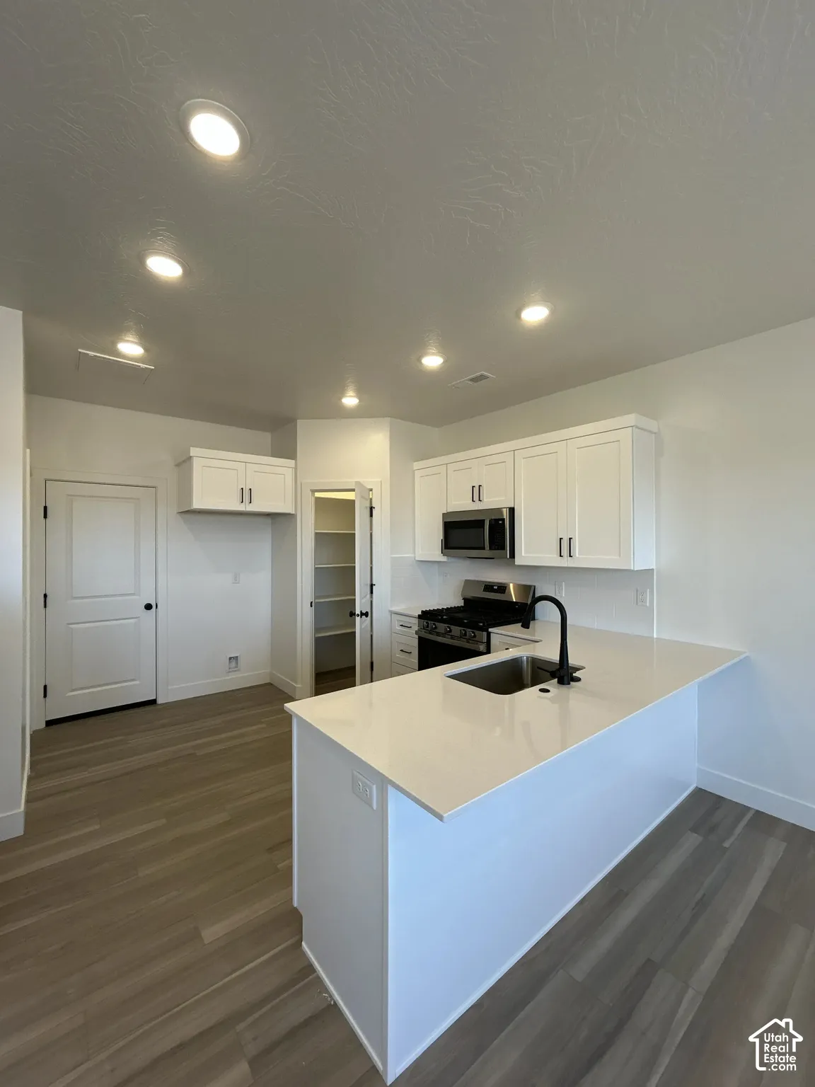Kitchen featuring white cabinetry, stainless steel appliances, wood-finish flooring, recessed lighting, and a kitchen island with a sink