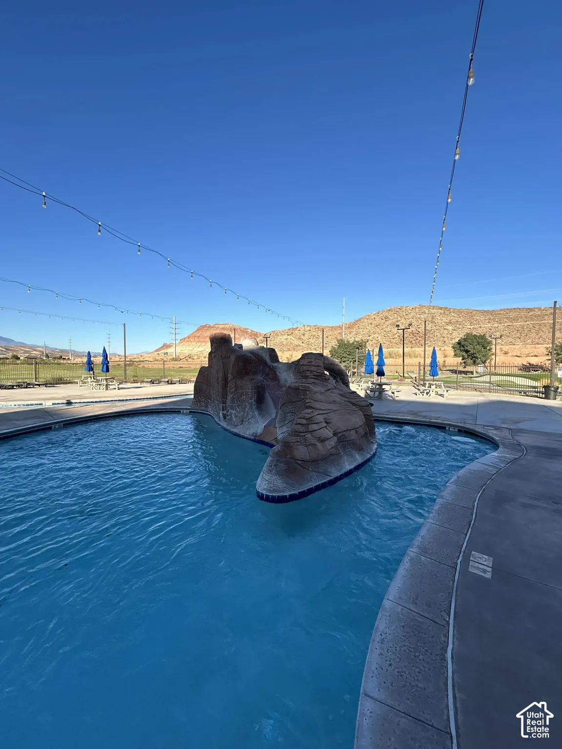 Swimming pool with a rock water feature, concrete pool deck, and string lighting