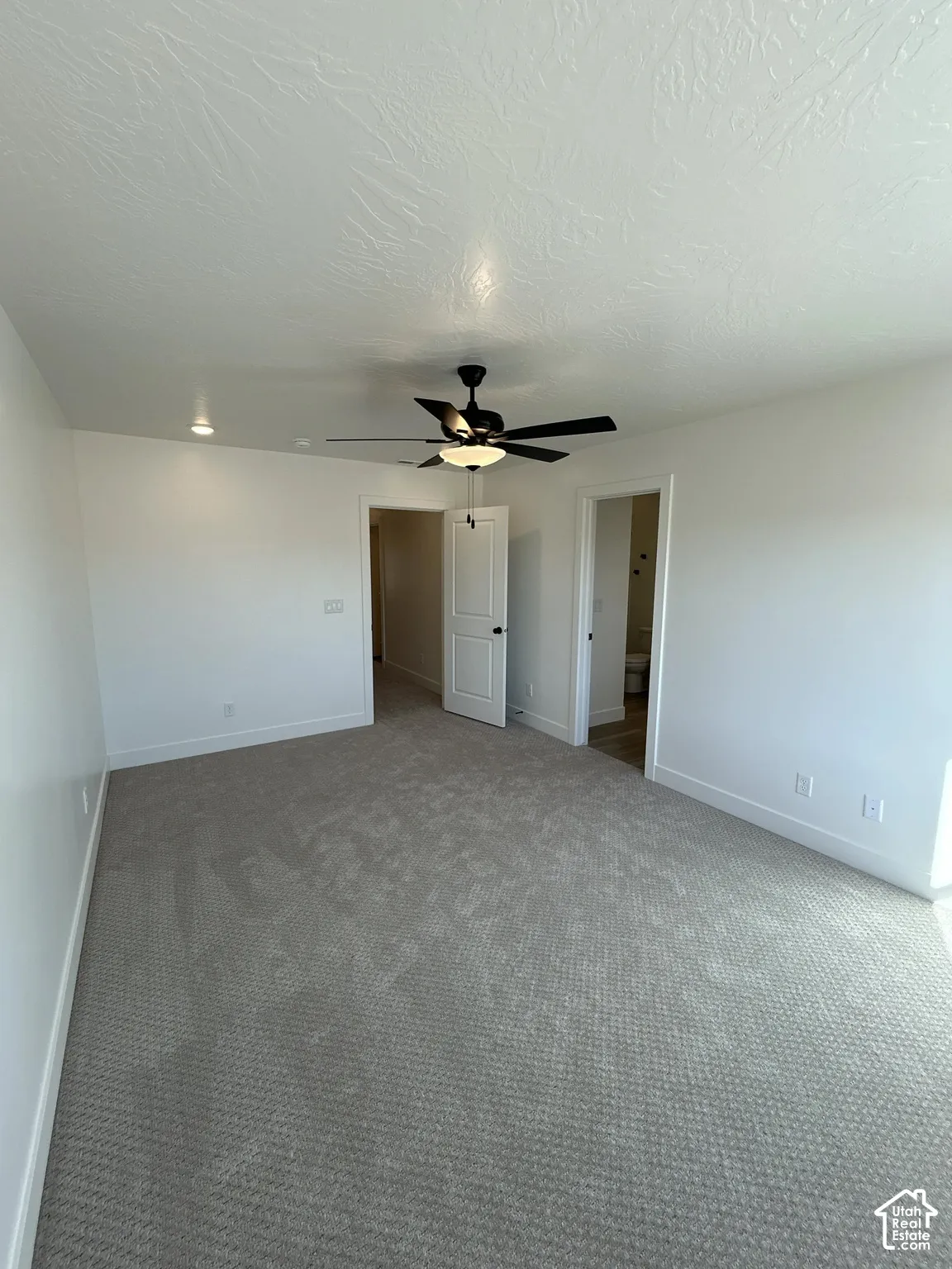 Spacious room featuring neutral carpeting, white walls, and a ceiling fan with integrated lighting