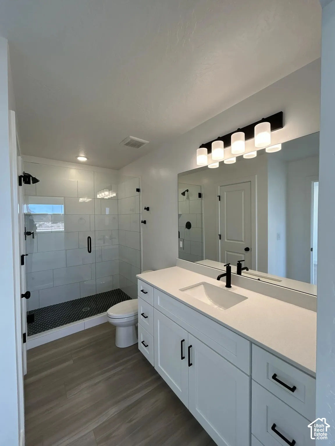 Double vanity with integrated sink, sleek black fixtures, white shaker cabinetry, and a glass-enclosed shower with subway tile surround and mosaic floor