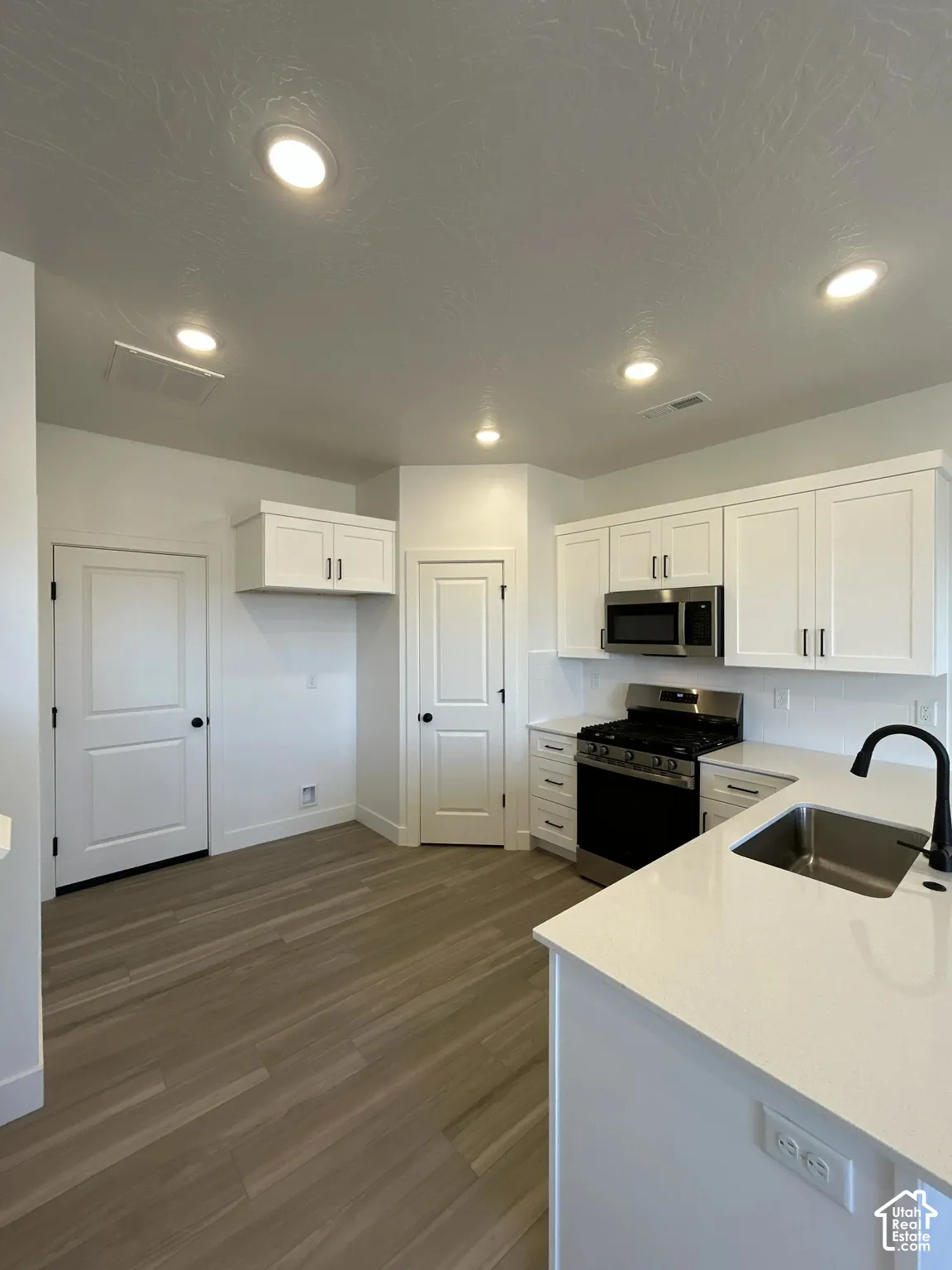 Kitchen featuring white cabinetry, stainless steel appliances, a single basin sink with a matte black faucet, recessed lighting, and wood-finish flooring