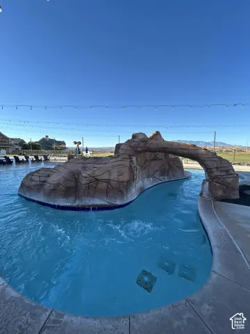 Resort-style pool with a rock formation, a water feature, and a paved deck surround