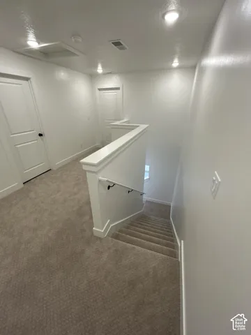 Carpeted landing with recessed lighting, white doors, and a wood-finish handrail descending to a lower level