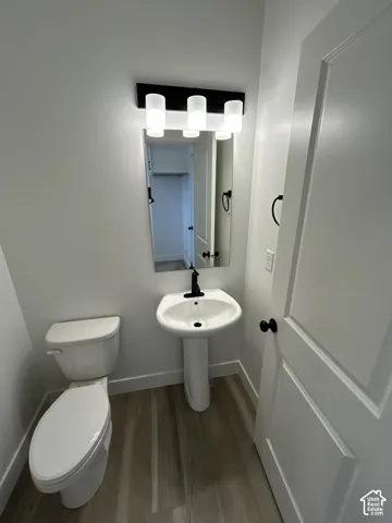 Pedestal sink with a matte black faucet, wall-mounted mirror, and wood-finish flooring