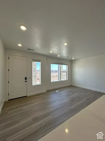 Recessed lighting, wood-finish flooring, multiple windows, white door, and a light-toned countertop