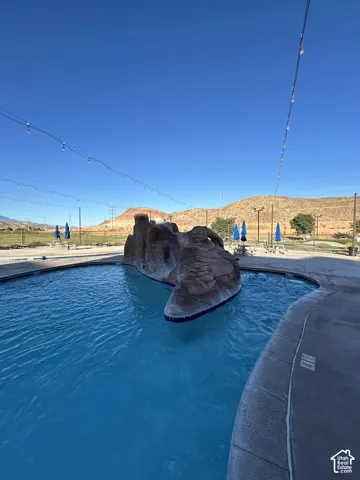 Swimming pool with a rock water feature, concrete pool deck, and string lighting