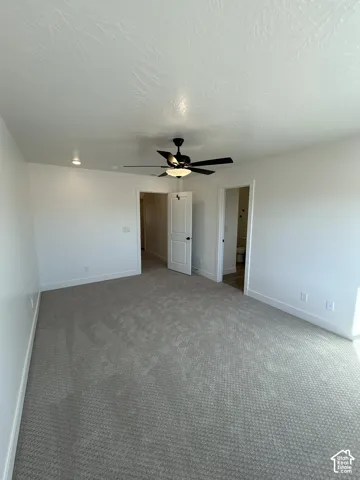 Spacious room featuring neutral carpeting, white walls, and a ceiling fan with integrated lighting