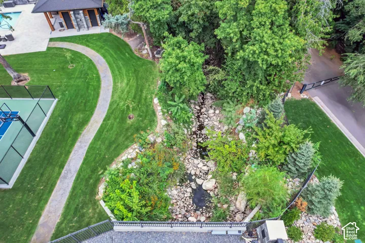 Landscaped grounds featuring a sport court, inground swimming pool, stone pathway, and a natural stream bed