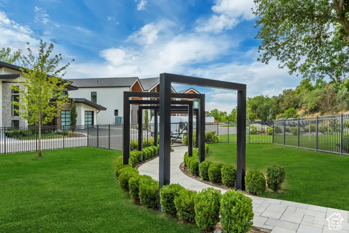 Expansive green lawn, paver pathway, decorative metal arbors, manicured shrubbery, and black perimeter fencing