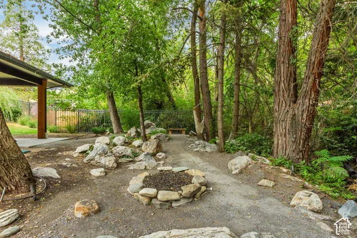 Stone-lined fire pit, gravel groundcover, mature trees, and covered patio area