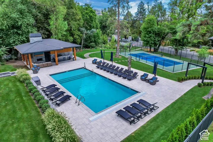 Expansive outdoor space featuring a rectangular swimming pool, paver patio, dedicated sports court, a covered outdoor kitchen, and manicured lawns