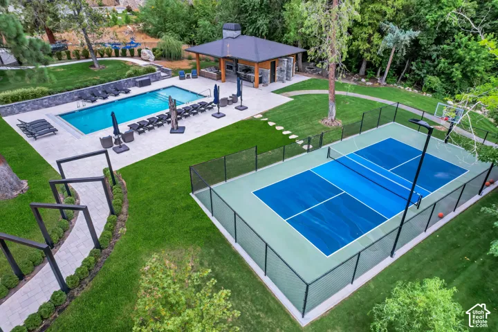 Outdoor swimming pool with expansive paved surround, a nearby covered outdoor structure, and a fenced multi-sport court