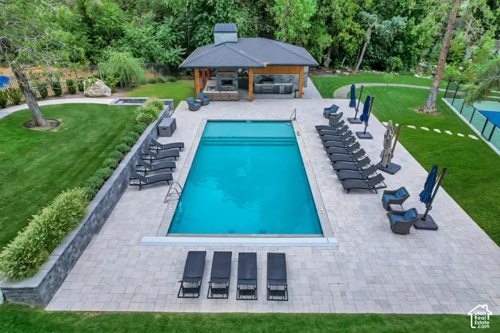 Outdoor oasis featuring a rectangular swimming pool, expansive paver patio, a built-in spa, a covered outdoor kitchen, and a tennis court