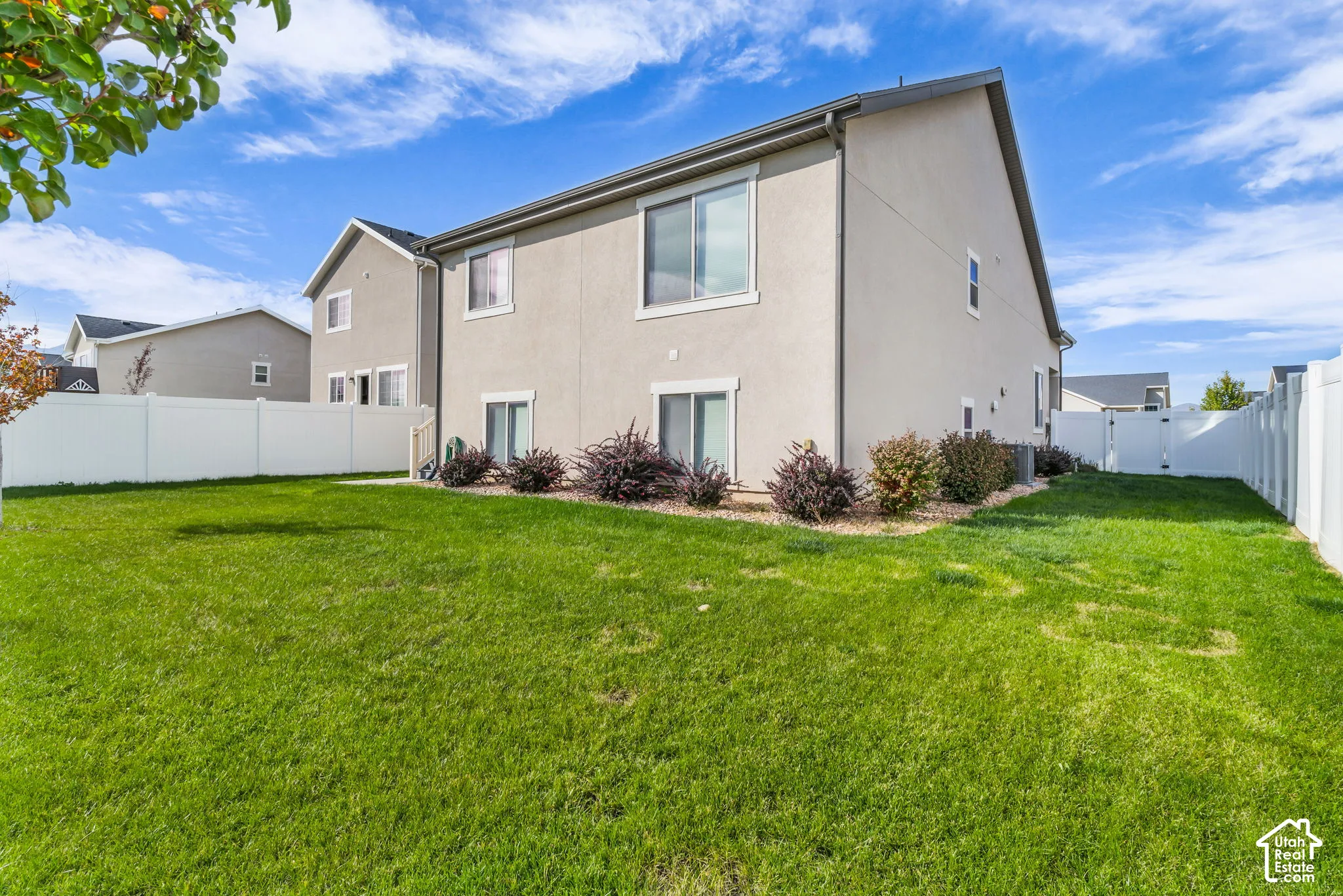 Expansive green lawn, white vinyl fencing, mature perimeter plantings, ground-level sliding glass doors, and upper-level windows
